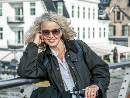 Kvinne med solbriller på en bro, holder en sykkel