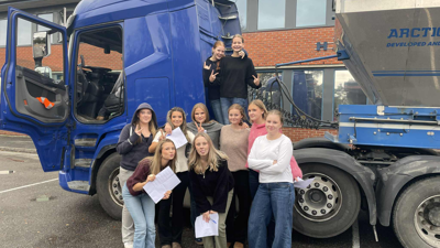 Mange jenter fra ungdomsskoletrinnet står foran en semitrailer. 