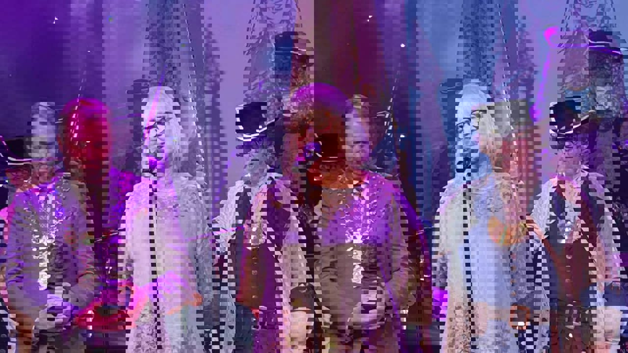 Tre personer står på en scene. En dame i forgrunnen snakker i mikrofon. 