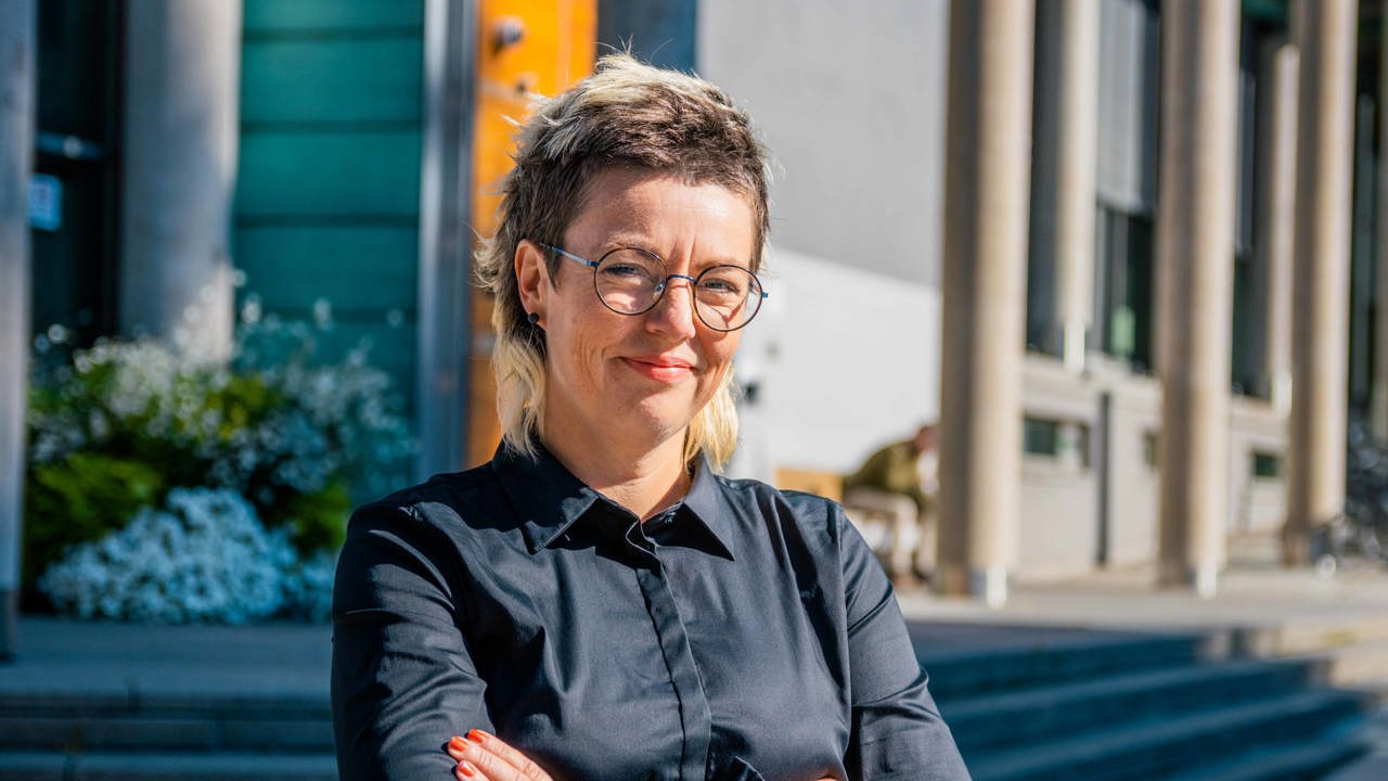 Profilbilde av kvinne som står med armene i kors og smiler til kamera. 