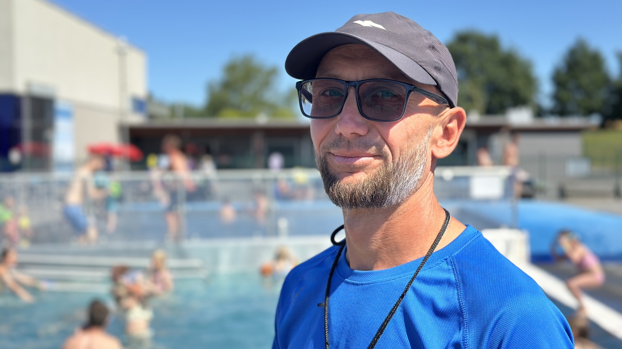 Ihor Tytarenko i badevaktuniform i solskinn ute med friluftsbadet uskarpt bak seg. Portrett.