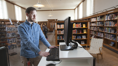Mann som står ved en pc på et bibliotek