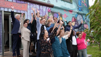 En stor gjeng jubler og løfter hendene i været foran en bygning 